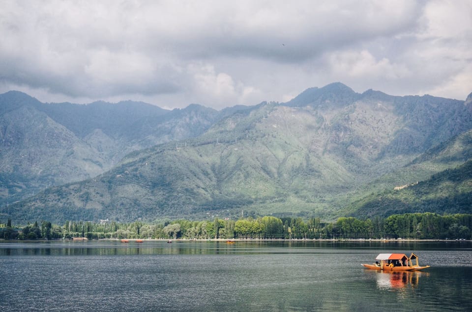 A shikara on calm water below the mountain slopes around Dal Lake.