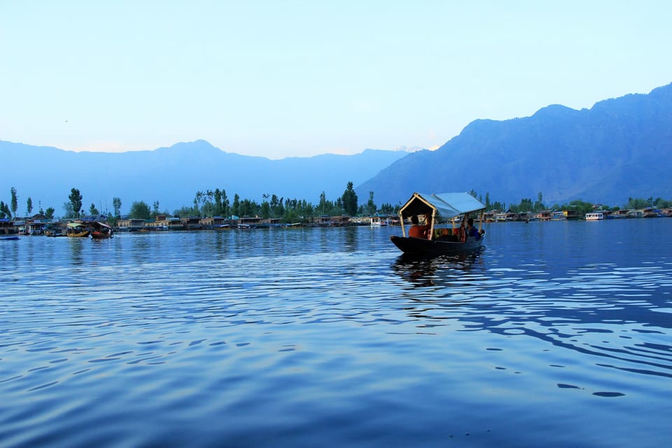 A shikara on blue water with mountain silhouettes across Dal Lake.