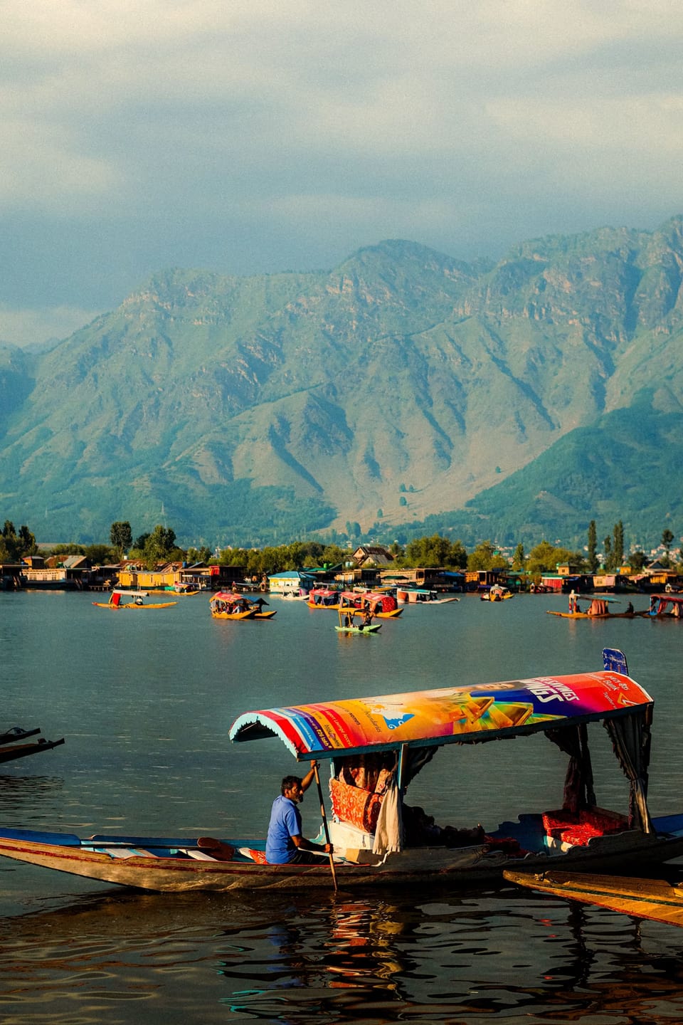 A brightly painted shikara in the foreground of a mountain view across Dal Lake.