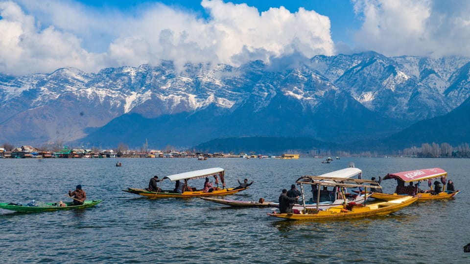 Boats crossing Dal Lake with snow-covered peaks in the distance.