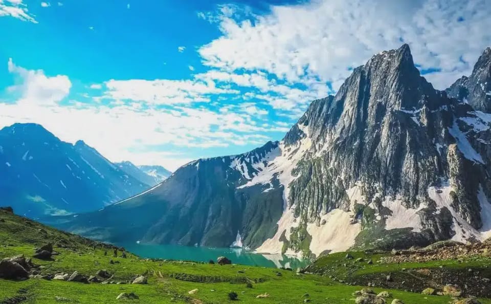 A green valley beneath dramatic rocky peaks and a blue sky.