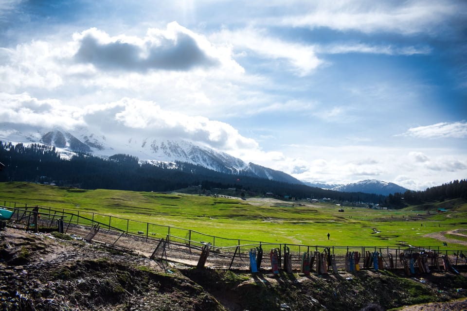 An open meadow and fences beneath cloud-covered mountains in Pahalgam.