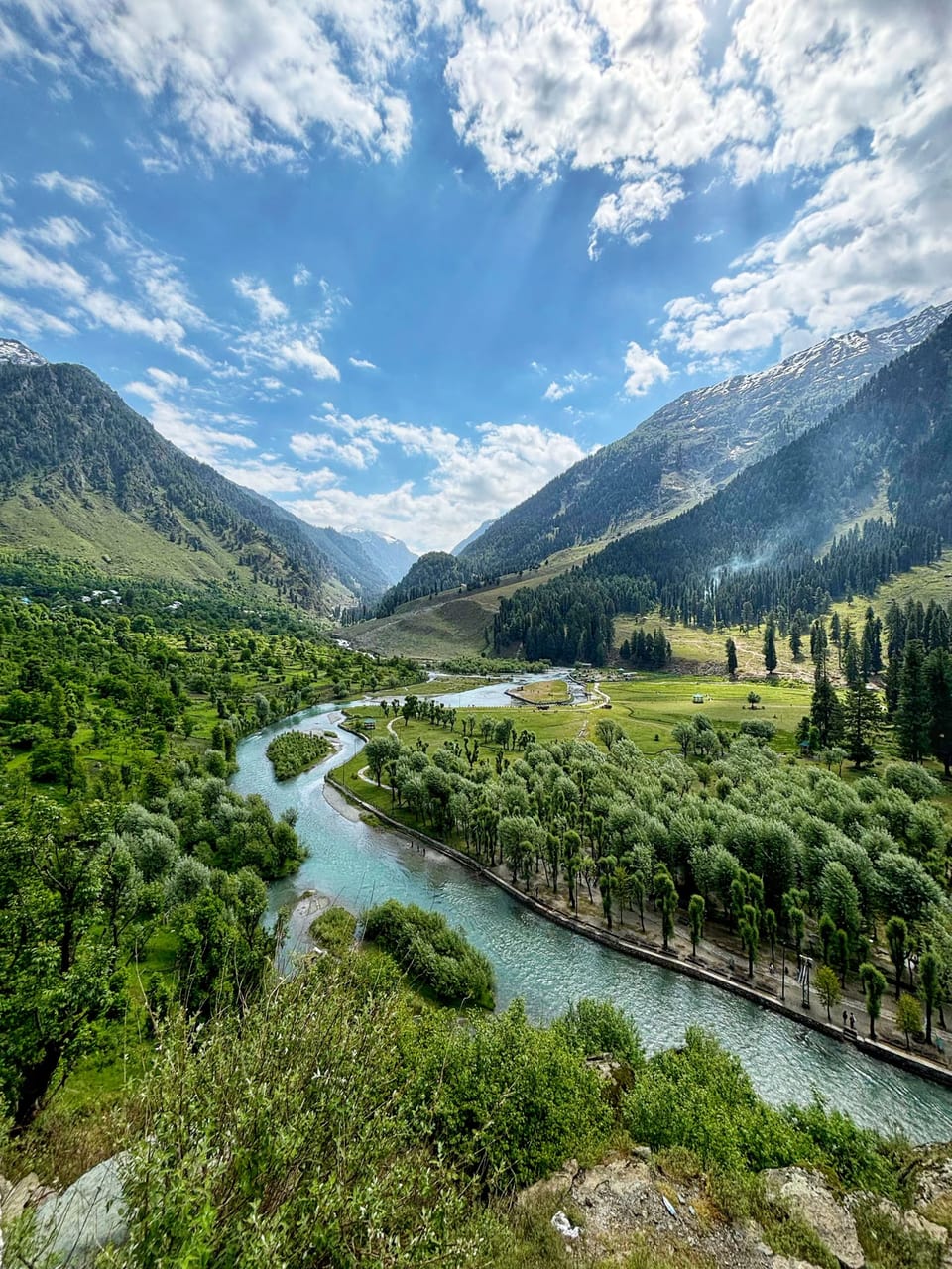 A winding river between forested slopes and mountains in Pahalgam.