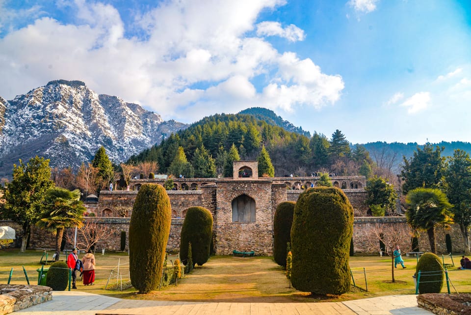 Stone arches and clipped garden trees at Pari Mahal with mountains behind.