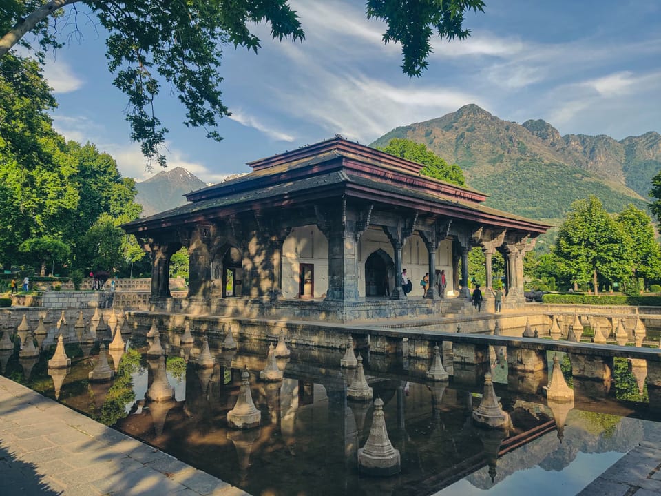 A stone garden pavilion reflected in water at Shalimar Garden.