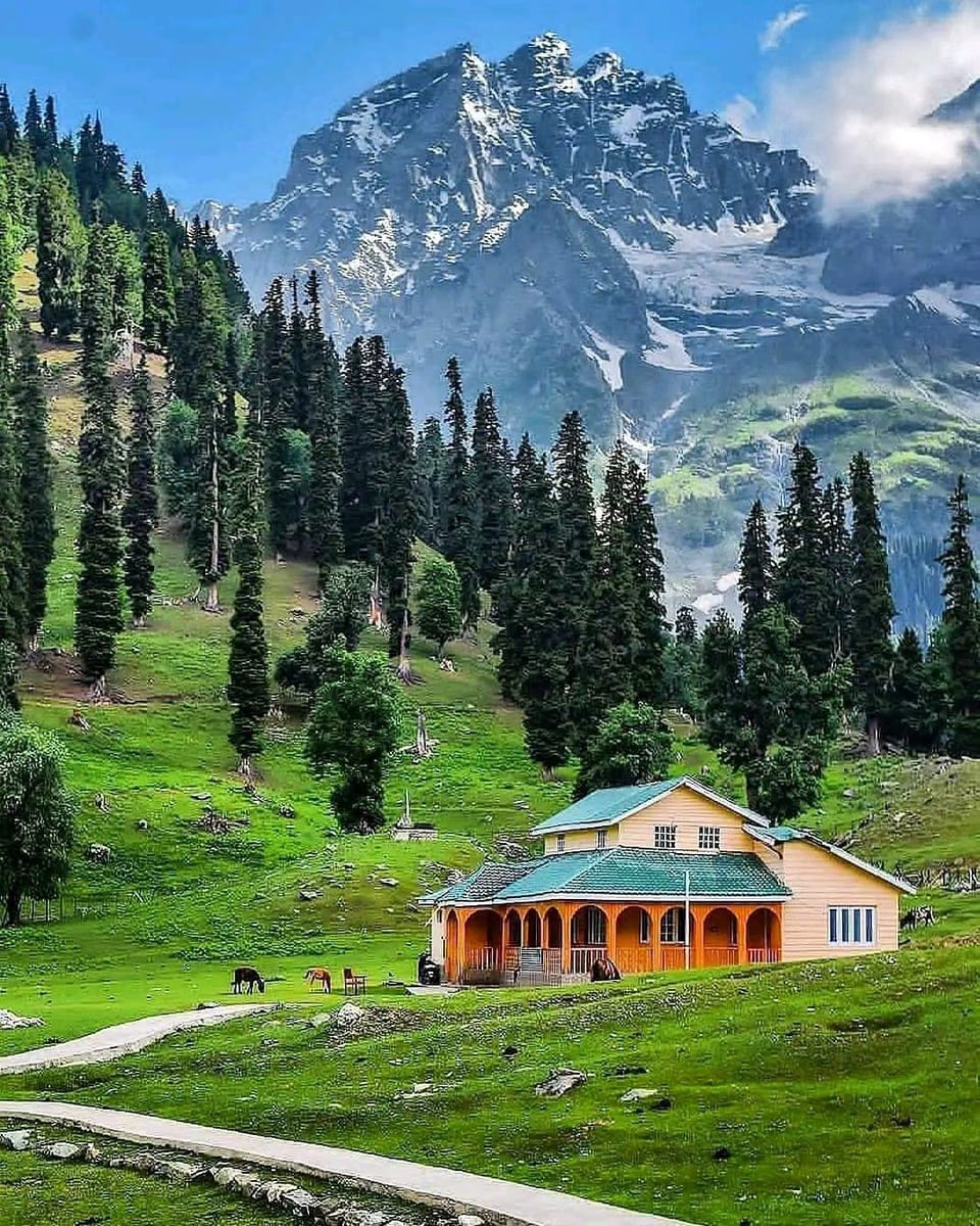 A small building beneath conifer-covered slopes and high peaks in Sonamarg.