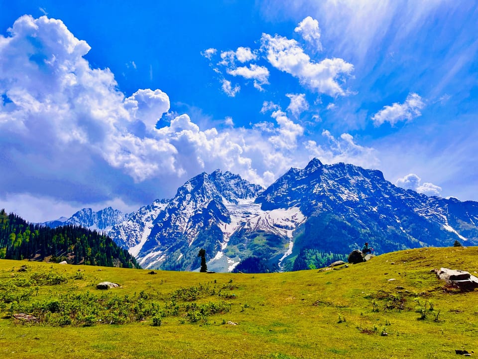 Snow-streaked peaks rising above open green meadows in Sonamarg.